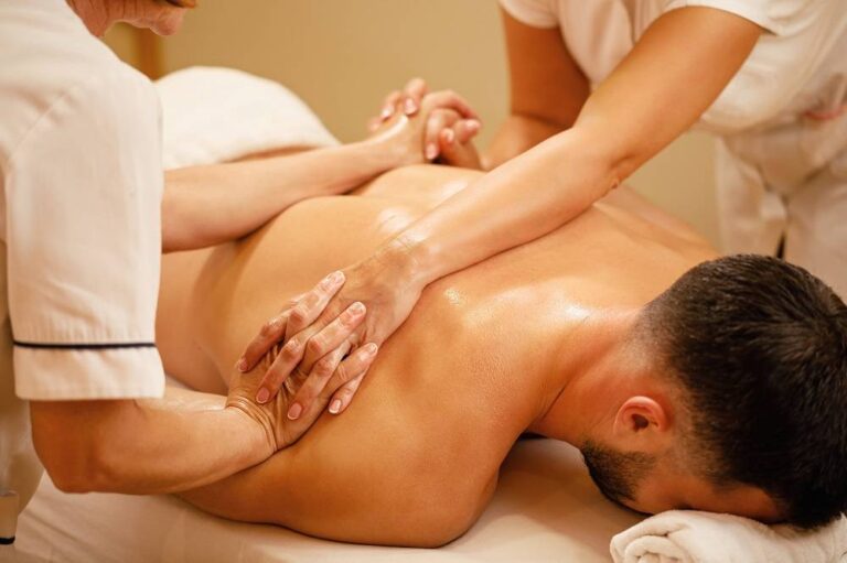 Female therapists holding hands while massaging back of a man at the spa